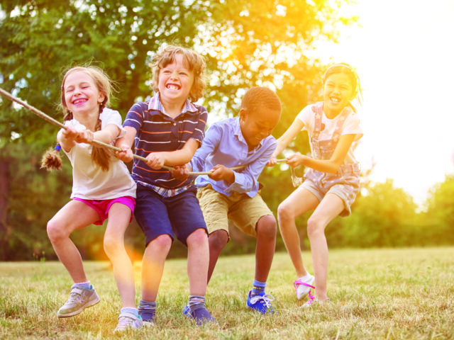 Multikulturelle Gruppe Kinder beim Tauziehen als Team in der Natur